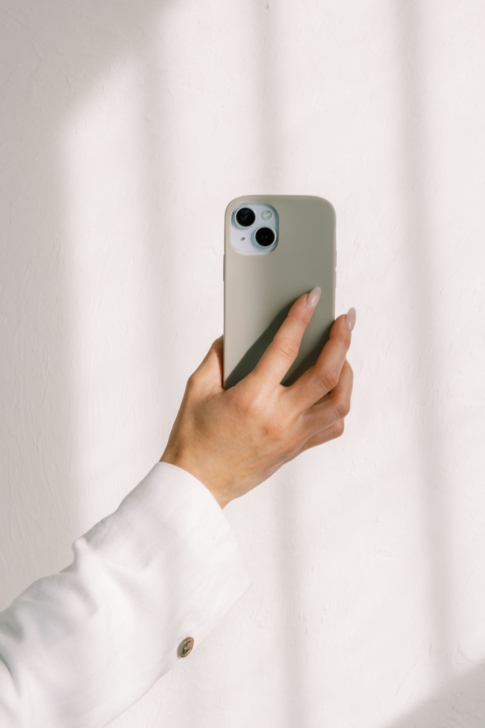 Woman holding phone in the air against a white background with striped shadows